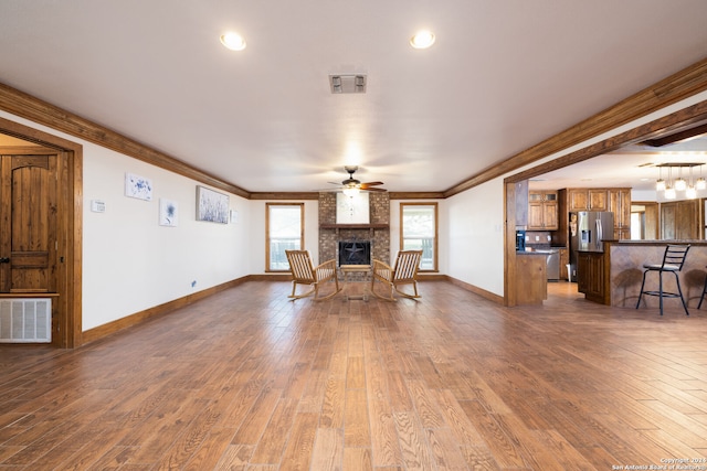 unfurnished living room featuring ceiling fan, hardwood / wood-style flooring, ornamental molding, and a brick fireplace