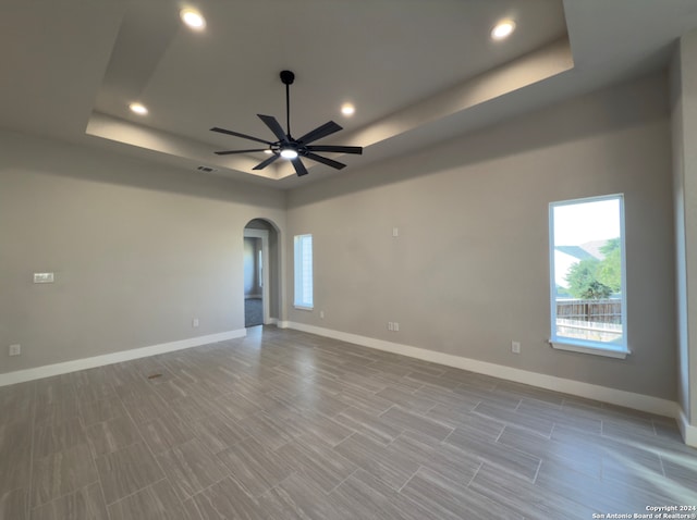 empty room with ceiling fan and a tray ceiling