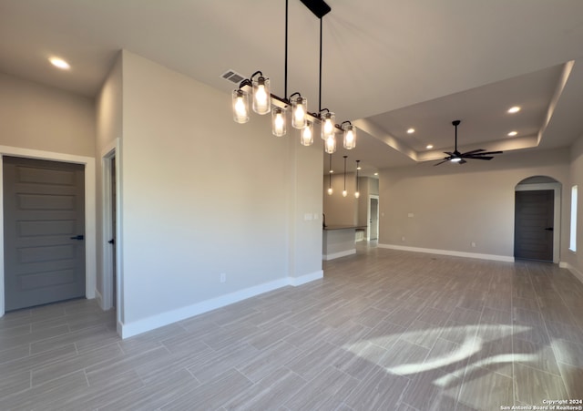 unfurnished living room with light tile patterned floors, a tray ceiling, and ceiling fan