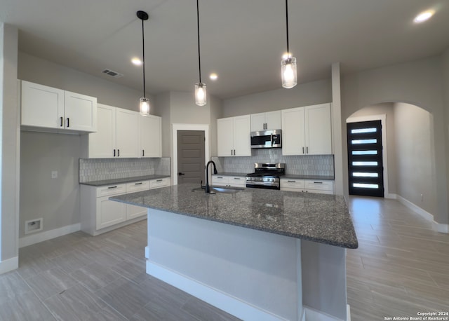 kitchen with appliances with stainless steel finishes, dark stone counters, sink, white cabinets, and an island with sink