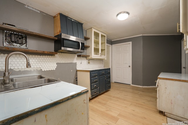 kitchen with tasteful backsplash, ornamental molding, sink, and light wood-type flooring