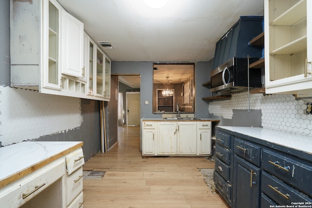 kitchen featuring tasteful backsplash, white cabinetry, light wood-type flooring, blue cabinetry, and sink