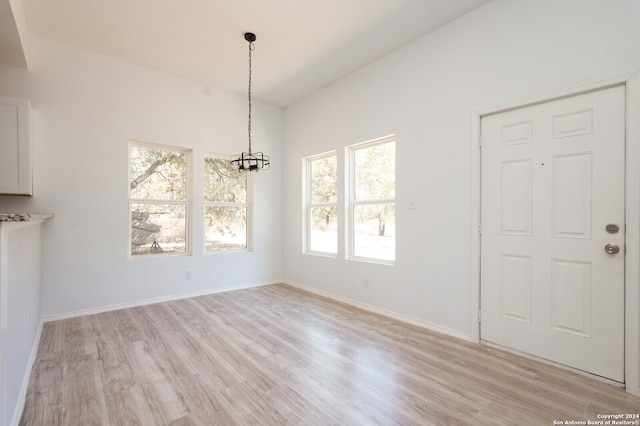 unfurnished dining area with a notable chandelier and light wood-type flooring