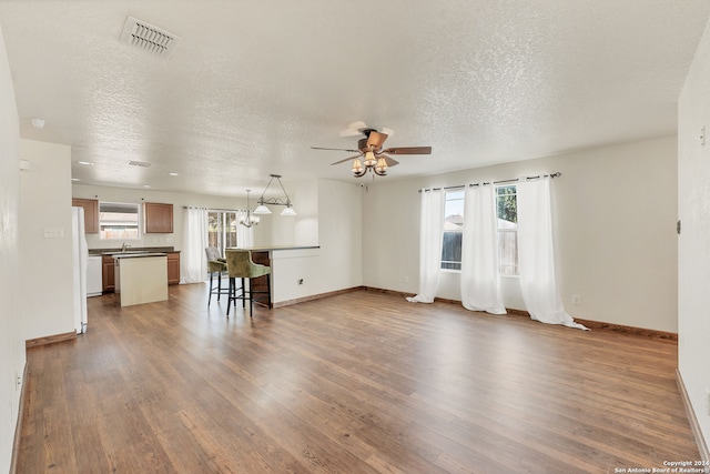 unfurnished living room featuring dark wood-type flooring, ceiling fan, a textured ceiling, and a wealth of natural light