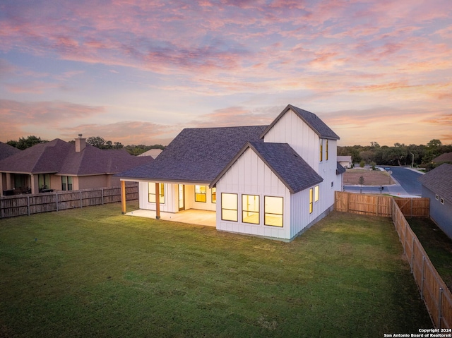 back house at dusk with a patio area and a lawn