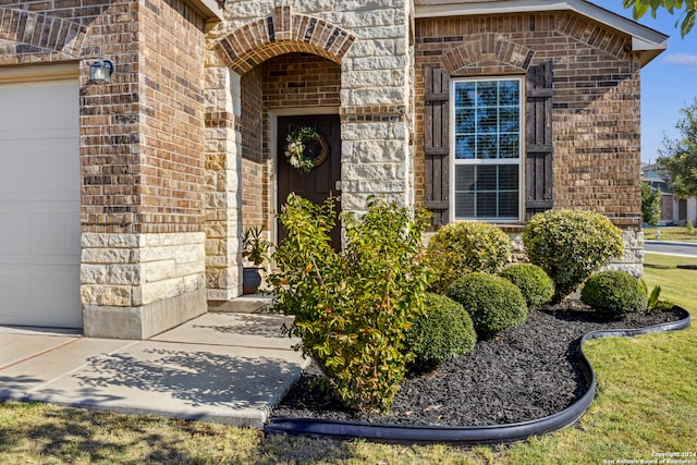 view of exterior entry with a garage and a lawn