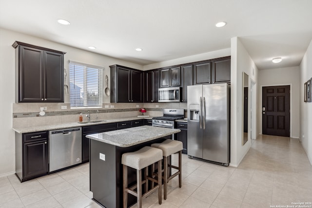 kitchen with a kitchen island, stainless steel appliances, dark brown cabinets, sink, and light stone counters