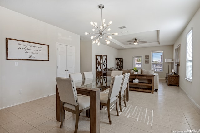 tiled dining area featuring a raised ceiling and ceiling fan with notable chandelier