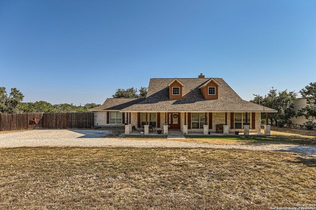 country-style home with a porch, fence, stone siding, and a chimney