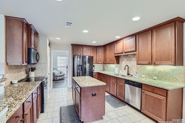 kitchen with tasteful backsplash, light stone countertops, appliances with stainless steel finishes, sink, and a kitchen island