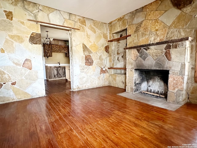 unfurnished living room featuring a notable chandelier, hardwood / wood-style flooring, sink, and a fireplace