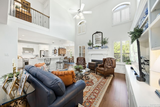 living room with a towering ceiling, ceiling fan, and dark hardwood / wood-style flooring