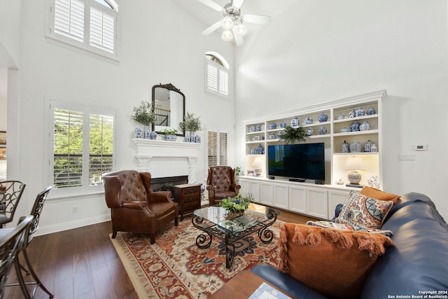 living room with a towering ceiling, dark wood-type flooring, and ceiling fan