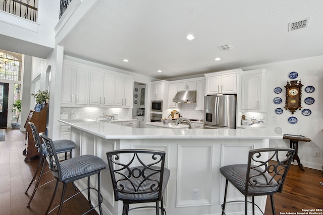 kitchen with appliances with stainless steel finishes, kitchen peninsula, white cabinets, and a breakfast bar area