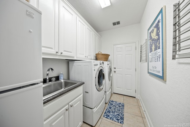 laundry room featuring cabinets, a textured ceiling, light tile patterned flooring, washing machine and dryer, and sink