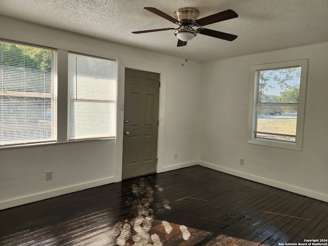 empty room featuring a textured ceiling, a healthy amount of sunlight, ceiling fan, and dark hardwood / wood-style flooring