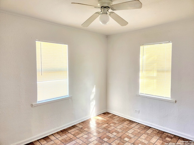 unfurnished room with brick patterned floor, a ceiling fan, and baseboards