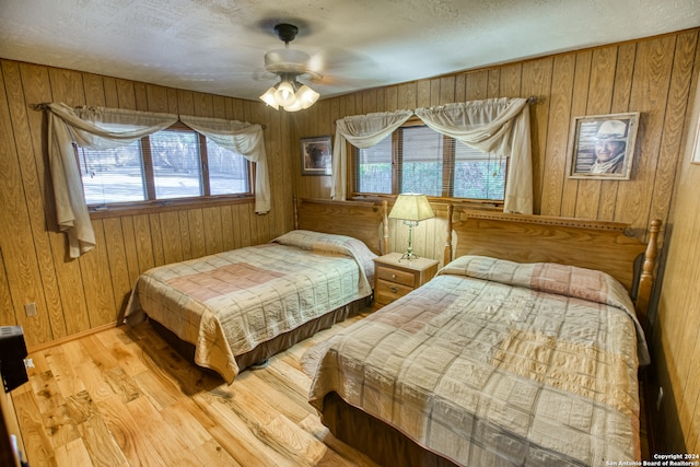 bedroom with wooden walls, multiple windows, light wood-type flooring, and ceiling fan