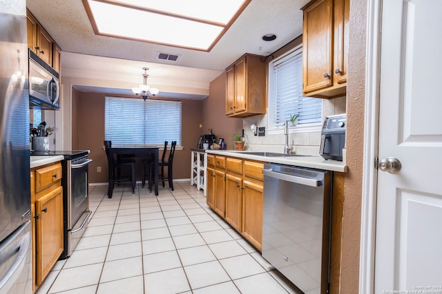 kitchen with appliances with stainless steel finishes, sink, a textured ceiling, light tile patterned floors, and an inviting chandelier