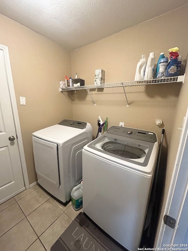 laundry area featuring a textured ceiling, light tile patterned flooring, and washing machine and clothes dryer