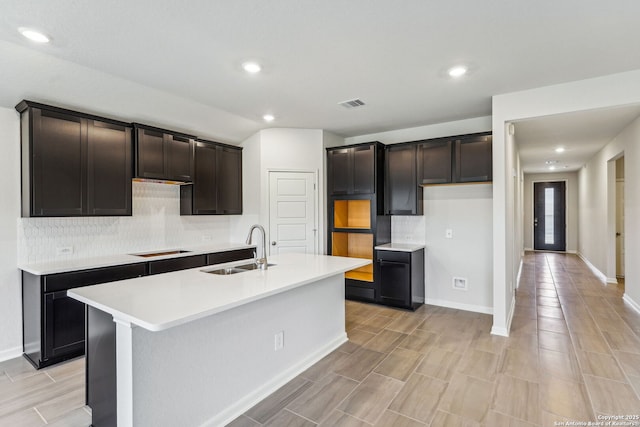 kitchen with an island with sink, sink, black electric cooktop, and decorative backsplash