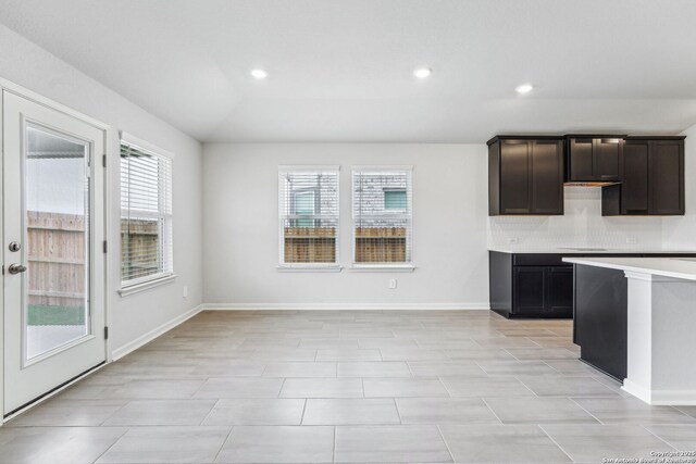 kitchen featuring dark brown cabinetry, backsplash, vaulted ceiling, and a healthy amount of sunlight