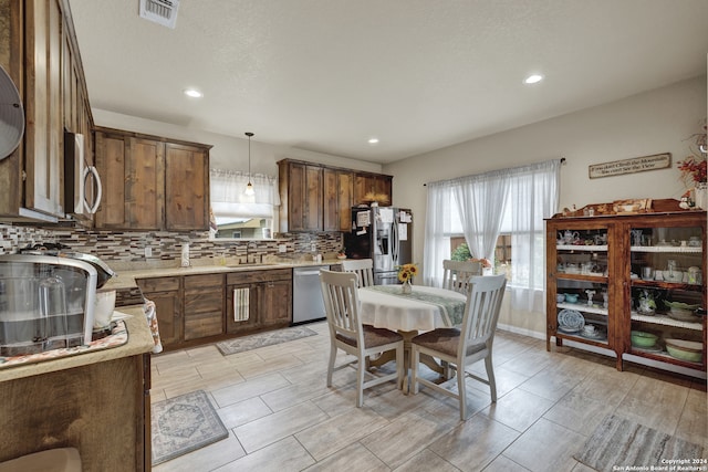 kitchen featuring sink, backsplash, stainless steel appliances, pendant lighting, and light hardwood / wood-style flooring