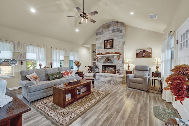 living room featuring a stone fireplace, high vaulted ceiling, light wood-type flooring, and ceiling fan