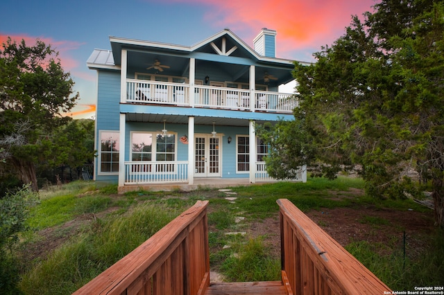 back house at dusk featuring ceiling fan, french doors, and a balcony