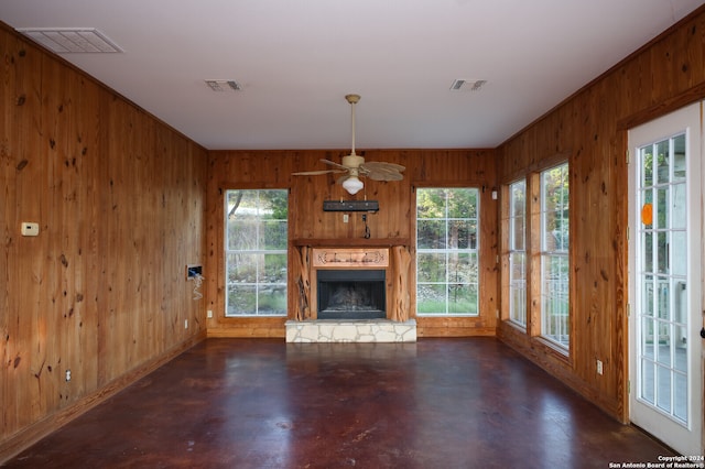 unfurnished living room featuring ceiling fan, a fireplace, and wooden walls