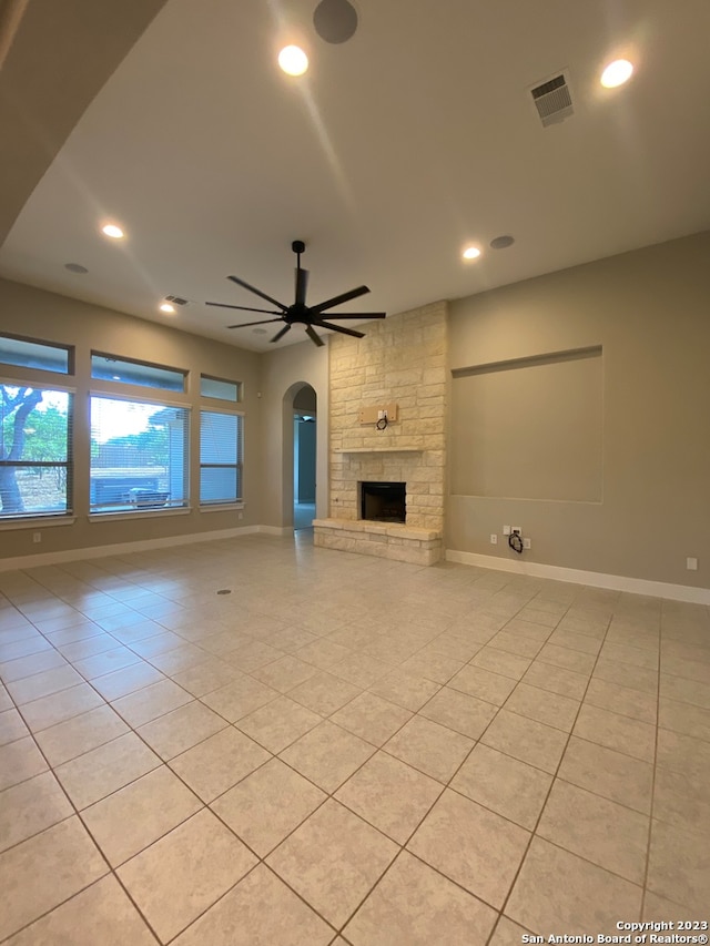 unfurnished living room featuring a stone fireplace, light tile patterned floors, and ceiling fan