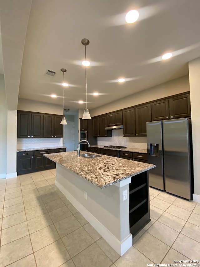 kitchen with light stone countertops, appliances with stainless steel finishes, sink, decorative light fixtures, and a center island with sink