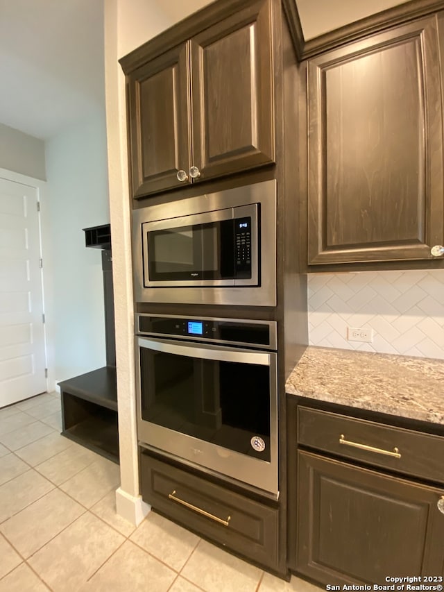 kitchen with dark brown cabinets, stainless steel appliances, light tile patterned flooring, light stone counters, and tasteful backsplash