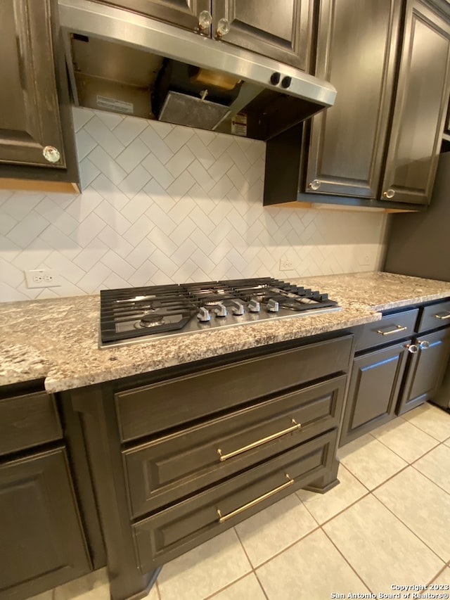 kitchen featuring stainless steel gas cooktop, dark brown cabinetry, light tile patterned floors, light stone counters, and tasteful backsplash