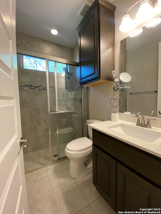 bathroom with a shower with door, vanity, toilet, and tile patterned flooring