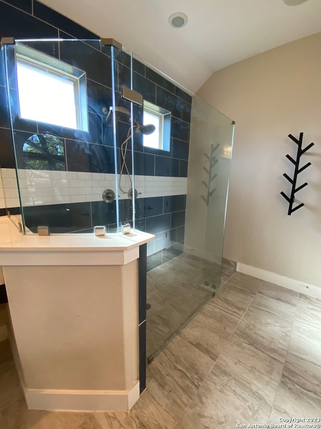 bathroom with a wealth of natural light, tile walls, lofted ceiling, and walk in shower