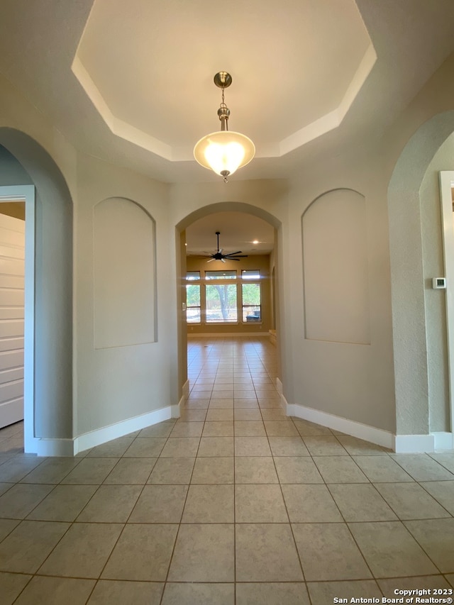 corridor featuring a tray ceiling and light tile patterned floors