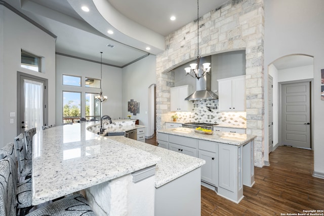 kitchen with a spacious island, a high ceiling, wall chimney range hood, dark hardwood / wood-style floors, and decorative light fixtures