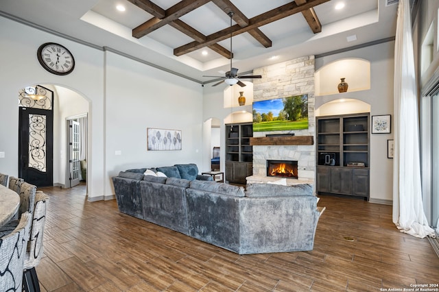 living room featuring dark wood-type flooring, coffered ceiling, a stone fireplace, and a towering ceiling