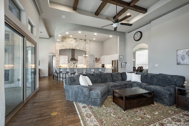 living room featuring ceiling fan with notable chandelier, beam ceiling, dark hardwood / wood-style flooring, and a high ceiling