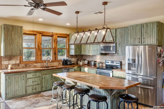 kitchen with a kitchen bar, sink, wooden counters, stainless steel appliances, and green cabinetry