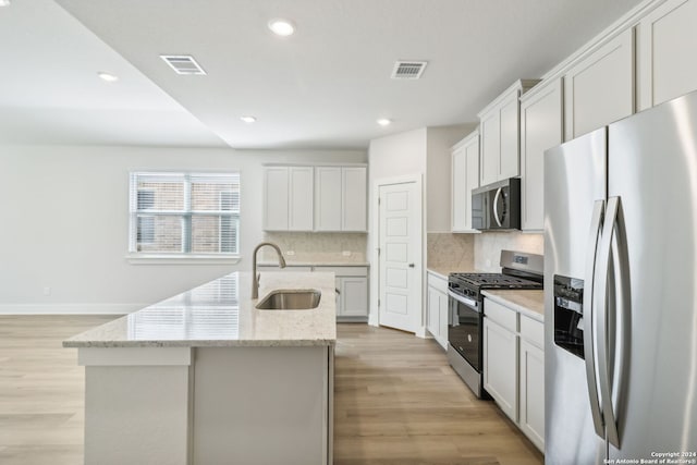 kitchen with light stone countertops, stainless steel appliances, sink, a center island with sink, and white cabinetry