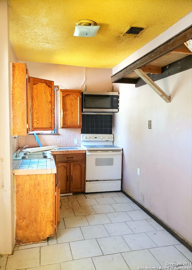 kitchen featuring tile counters, white electric range, backsplash, sink, and a textured ceiling