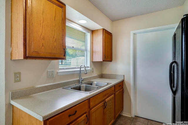 kitchen with sink, light tile patterned flooring, a textured ceiling, and black refrigerator