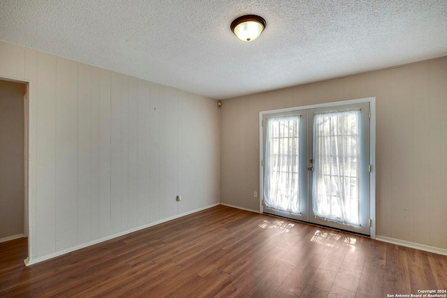 empty room with french doors, dark wood-type flooring, a textured ceiling, and wooden walls