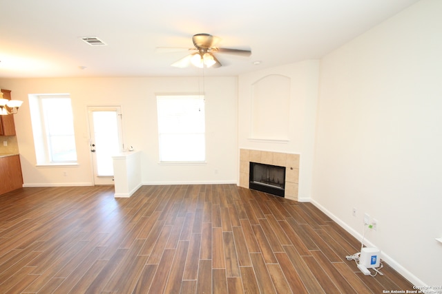 unfurnished living room featuring dark wood-type flooring, ceiling fan, a fireplace, and plenty of natural light