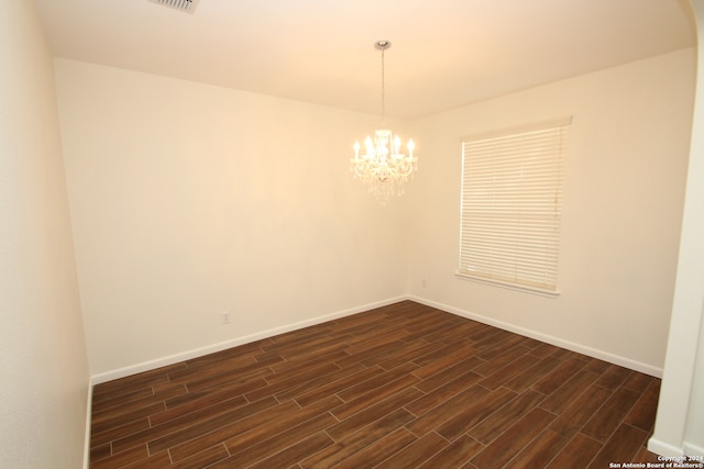 empty room with a notable chandelier and dark hardwood / wood-style floors