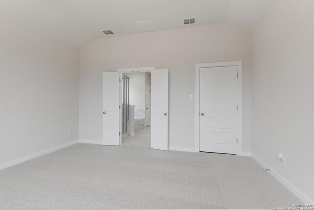 unfurnished bedroom featuring lofted ceiling, ensuite bathroom, and light carpet