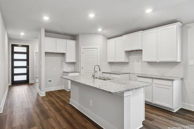 kitchen featuring sink, white cabinetry, backsplash, light stone countertops, and an island with sink