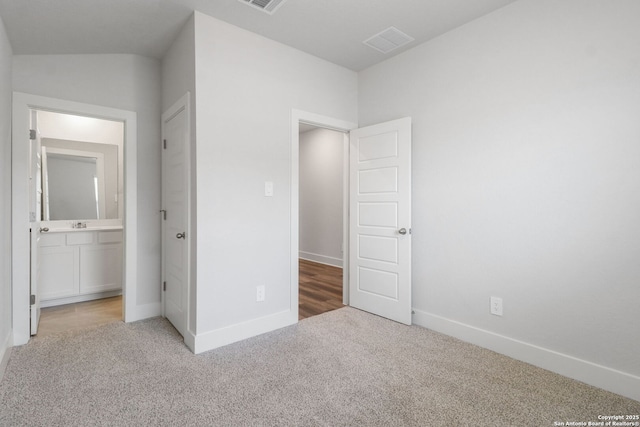 unfurnished bedroom featuring light colored carpet and ensuite bathroom